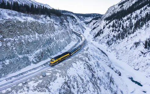 Aurora Winter Train traveling through snowy Alaskan mountains on the Alaska Railroad.
