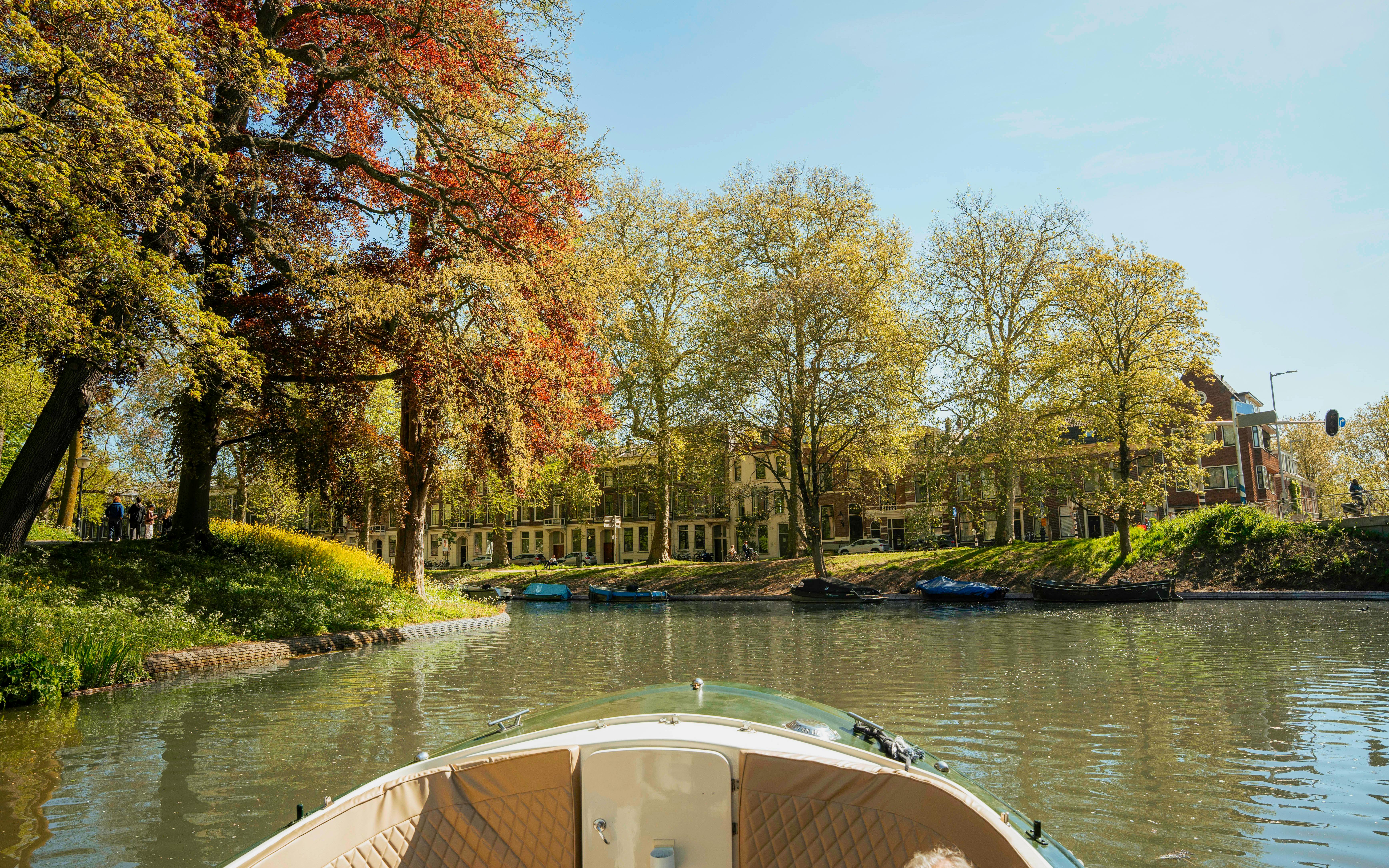 Utrecht canal view from open boat with trees and historic buildings.