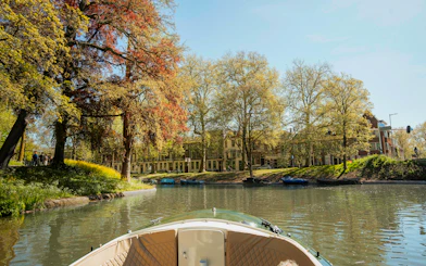 Utrecht canal view from open boat with trees and historic buildings.
