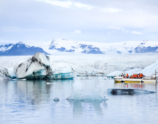 Tourists on a boat tour in Jokulsarlon, Iceland, surrounded by floating icebergs.