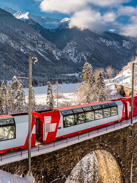 Glacier Express train crossing a snowy bridge in the Swiss Alps.