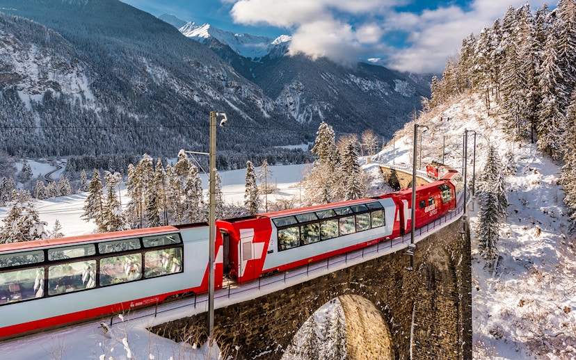 Glacier Express train crossing a snowy bridge in the Swiss Alps.