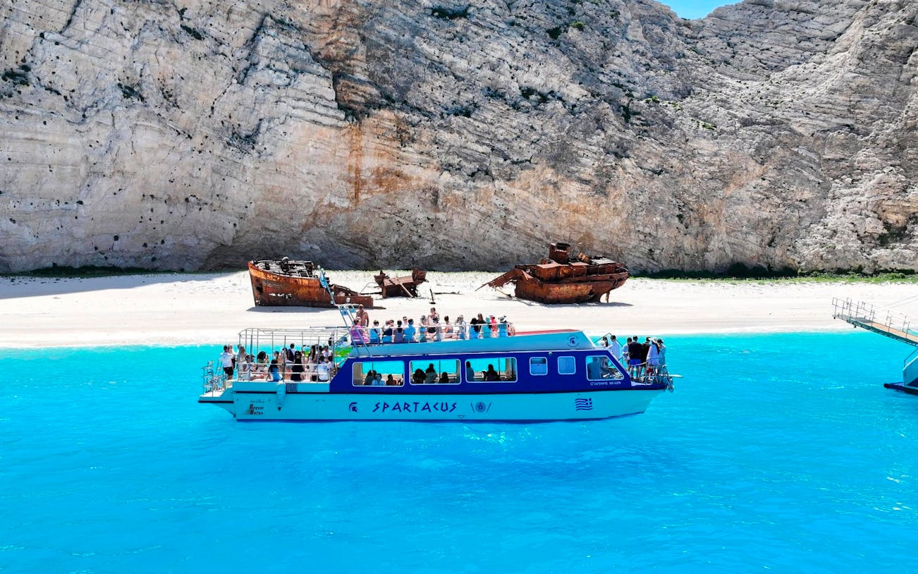 Glass bottom boat near Navagio Beach with shipwreck in background, Zakynthos, Greece.