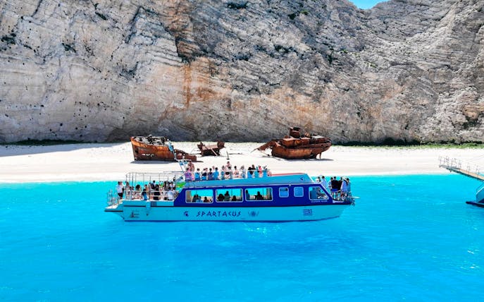 Glass bottom boat near Navagio Beach with shipwreck in background, Zakynthos, Greece.