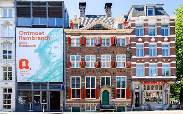 Exteriors of the Rembrandt House Museum in Amsterdam with red shutters and historic architecture.