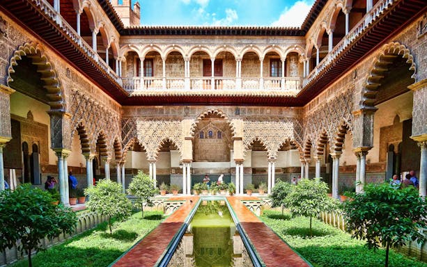 Courtyard of Alcazar Seville with intricate arches and lush greenery.