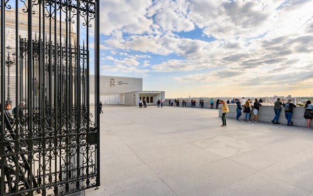 Visitors at Madrid Royal Palace terrace with city view, near Royal Collections Gallery.