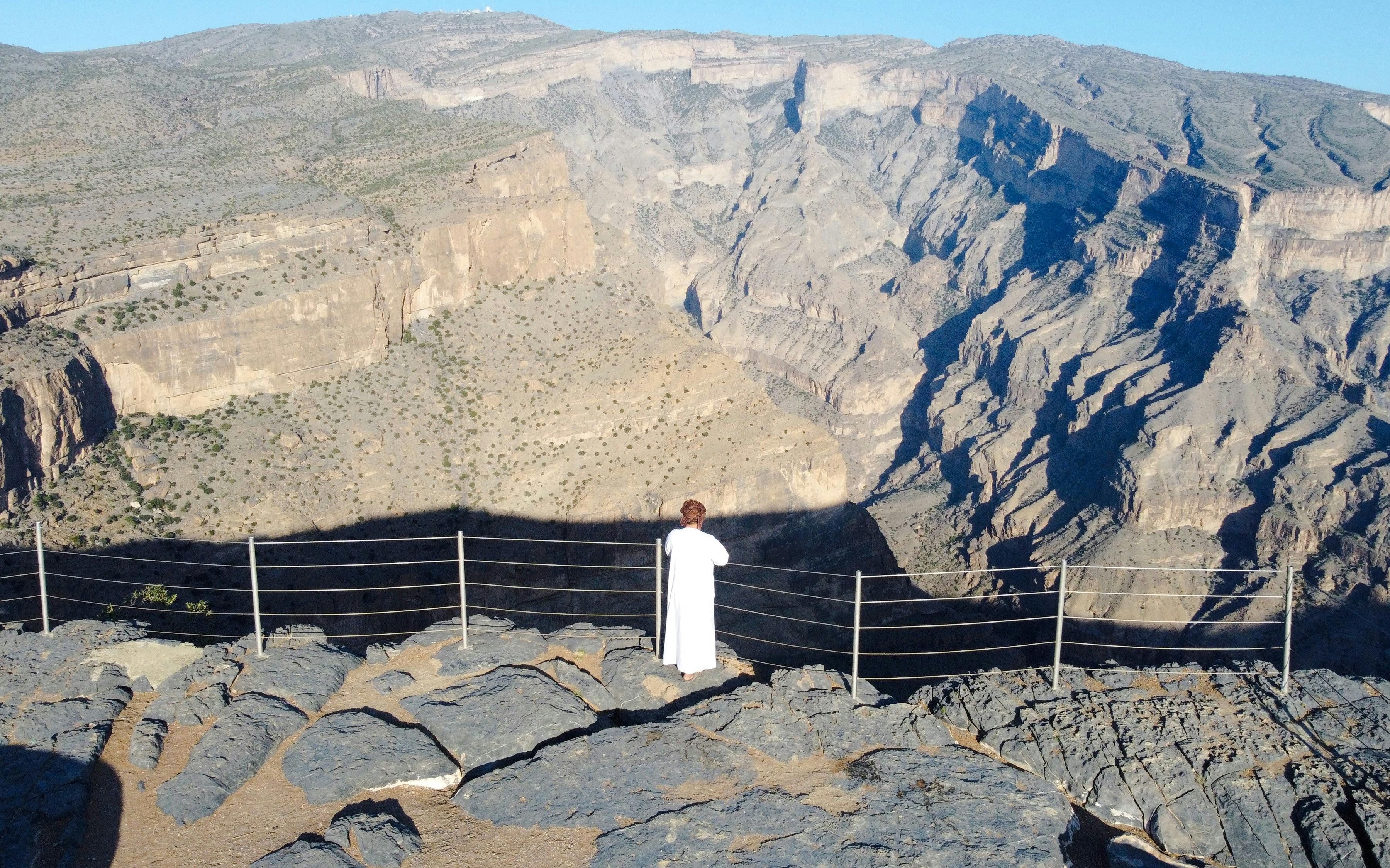 Visitor overlooking the Oman Grand Canyon from a rocky viewpoint.