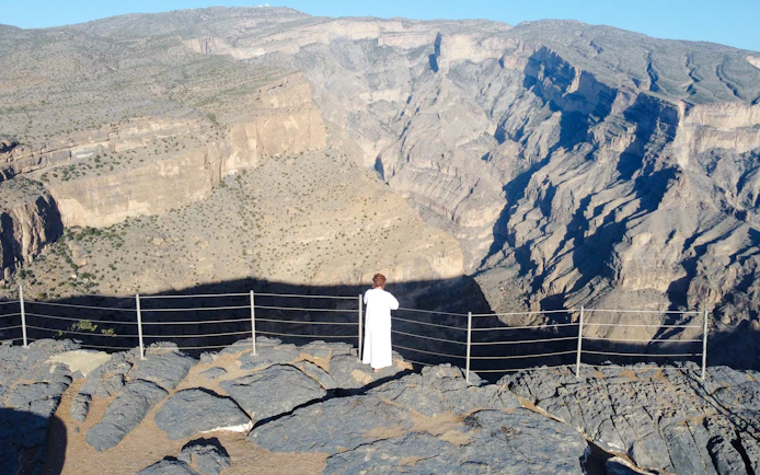 Visitor overlooking the Oman Grand Canyon from a rocky viewpoint.