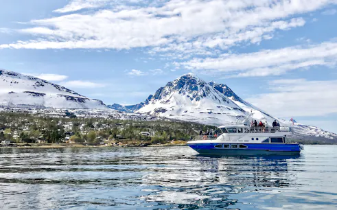 Cruise boat on a polar fjord with snowy mountains in the background.