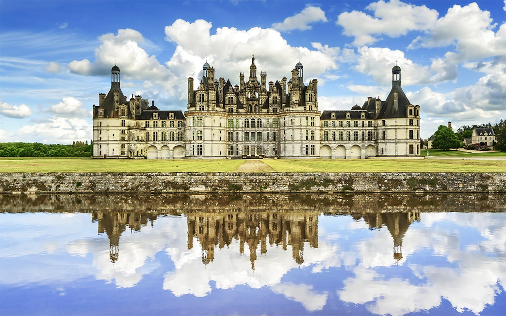 Château de Chambord reflecting in water under a blue sky, Loire Valley, France.