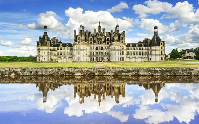 Château de Chambord reflecting in water under a blue sky, Loire Valley, France.