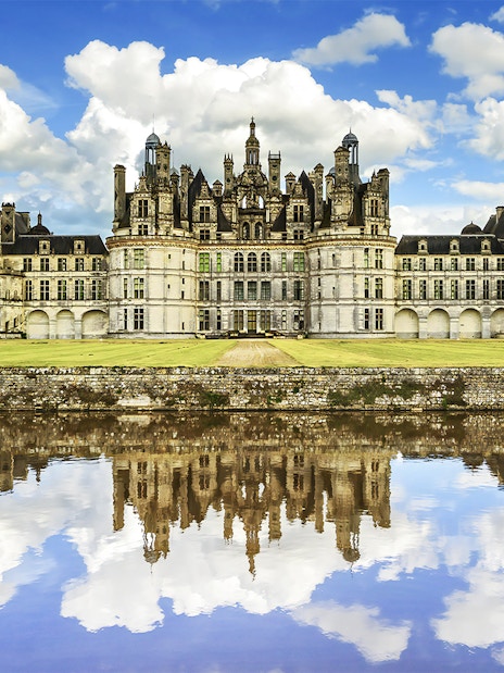Château de Chambord reflecting in water under a blue sky, Loire Valley, France.