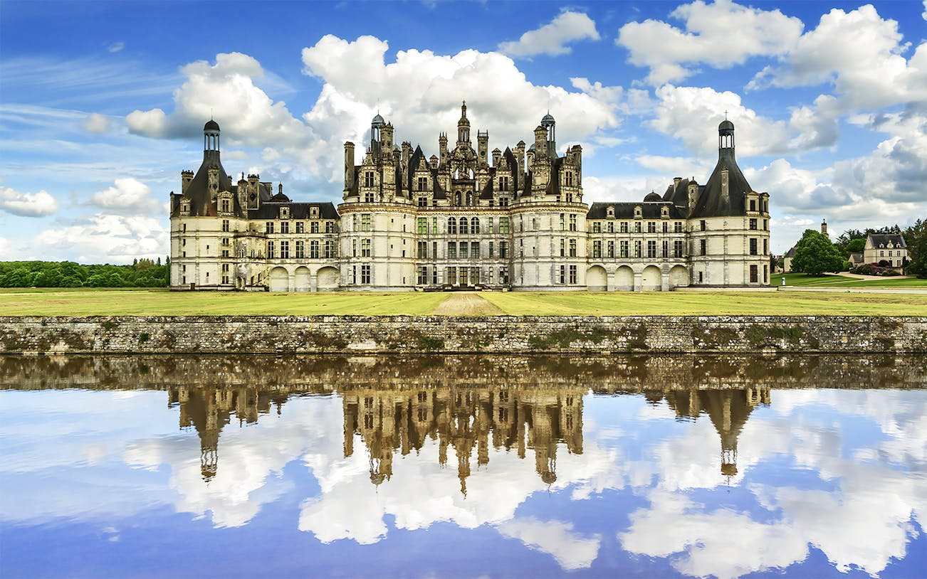 Château de Chambord reflecting in water under a blue sky, Loire Valley, France.