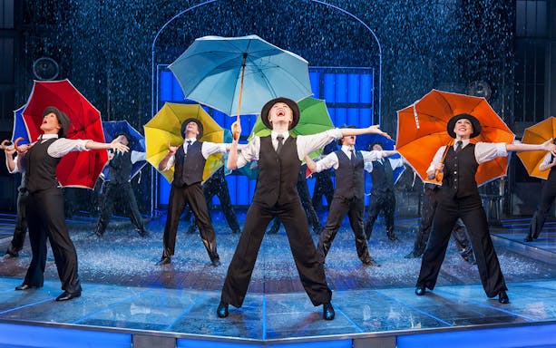 Performers with colorful umbrellas in a "Singin’ in the Rain" stage scene.