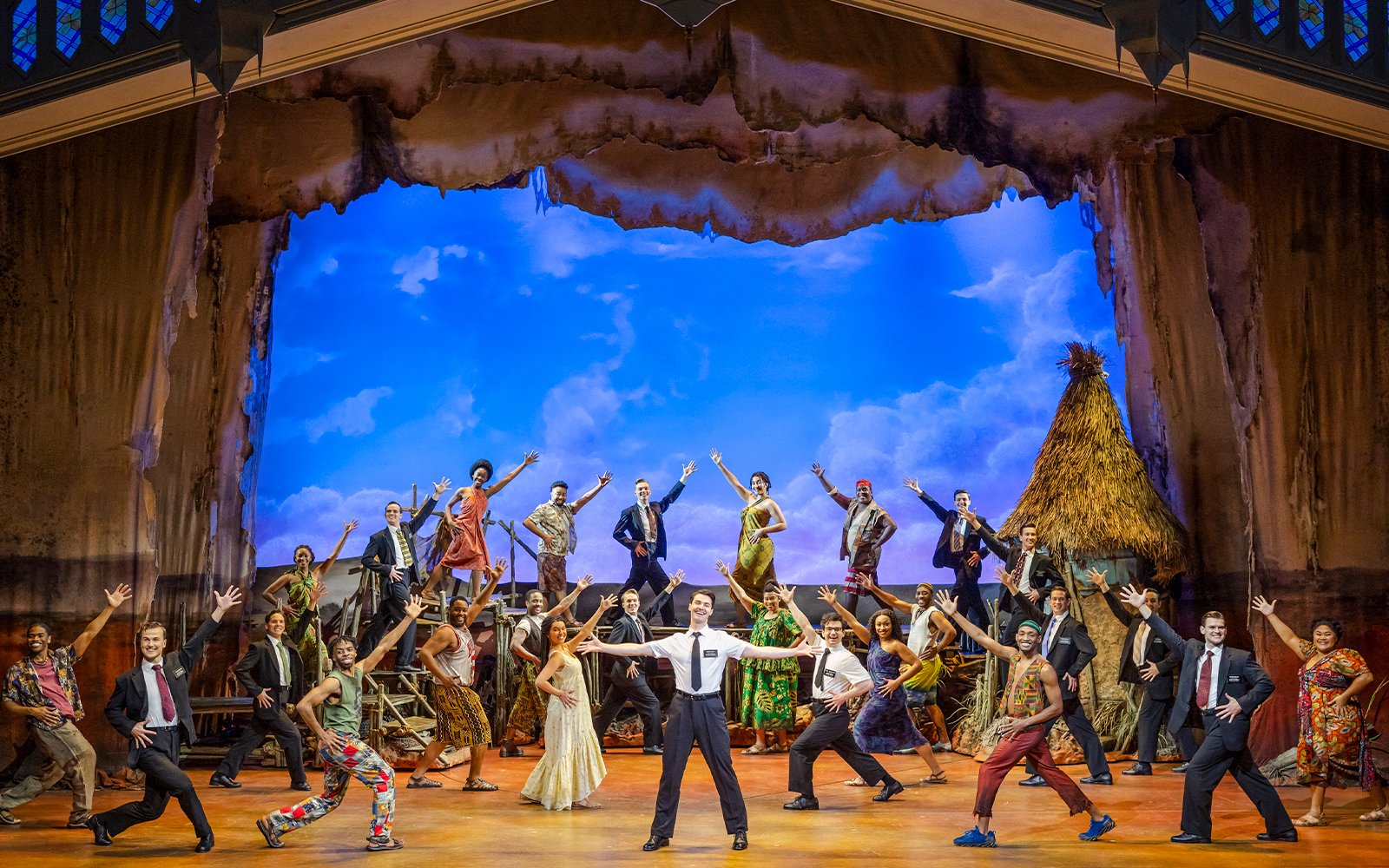 Stage performance of The Book of Mormon cast in Brisbane, featuring vibrant costumes and dynamic poses.