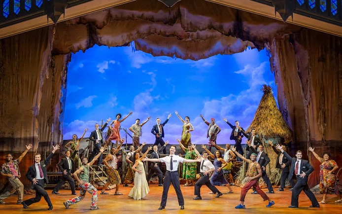 Stage performance of The Book of Mormon cast in Brisbane, featuring vibrant costumes and dynamic poses.