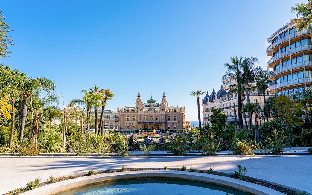Monaco Casino with gardens and palm trees on a sunny day.