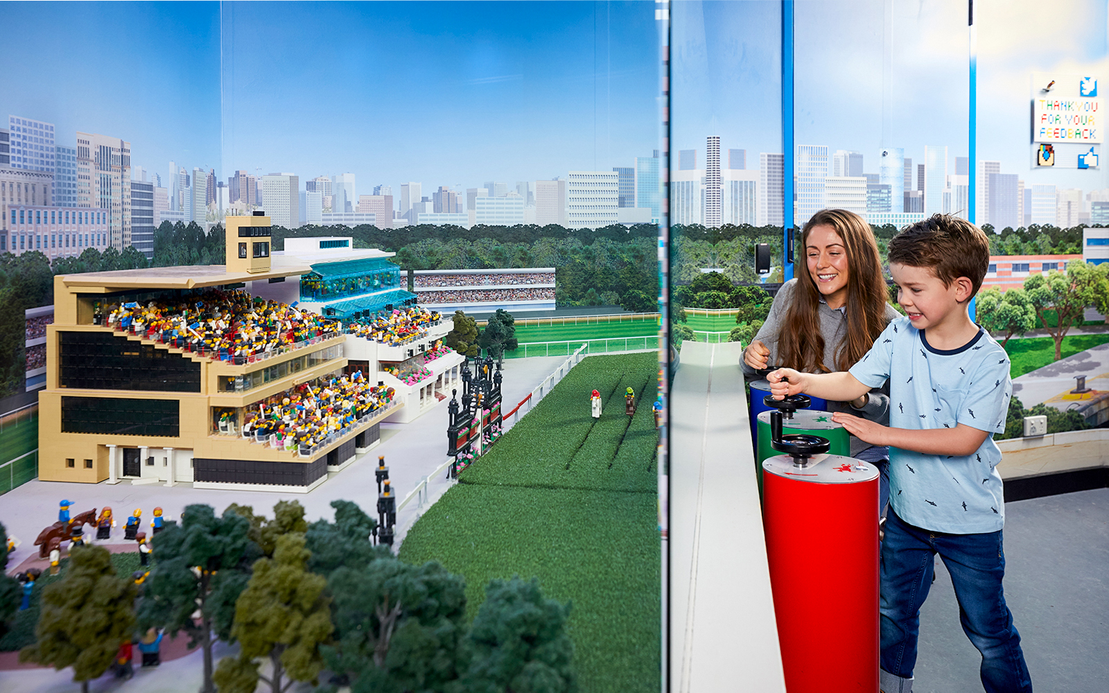 Child and adult interacting with LEGO racetrack model at LEGOLAND Discovery Centre.