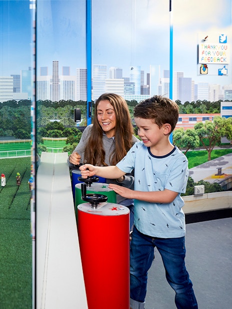 Child and adult interacting with LEGO racetrack model at LEGOLAND Discovery Centre.