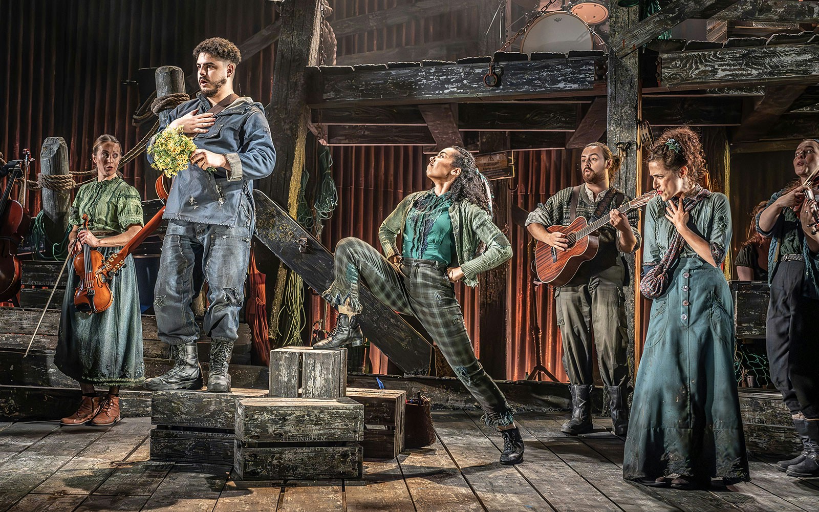 Cast performing on stage in "The Curious Case of Benjamin Button - The Musical" with instruments and dynamic poses.