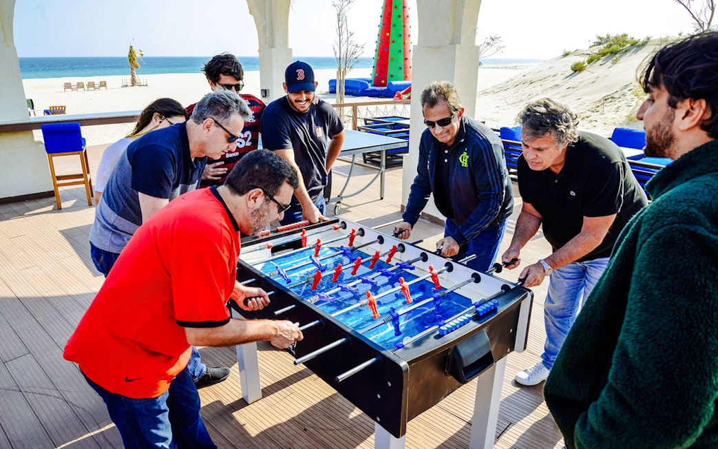 Tourists playing foosball at Al Majles Resort with beach view in the background.