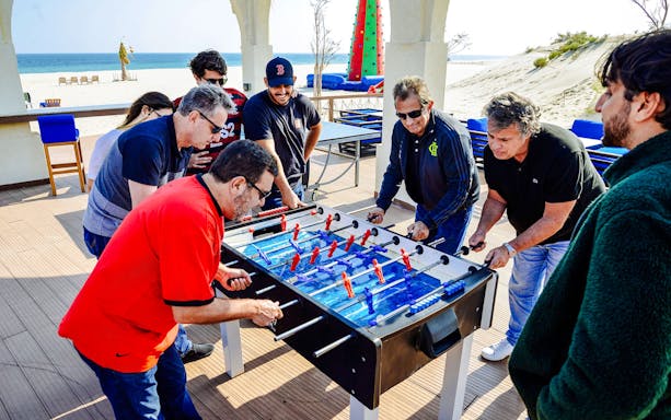 Tourists playing foosball at Al Majles Resort with beach view in the background.