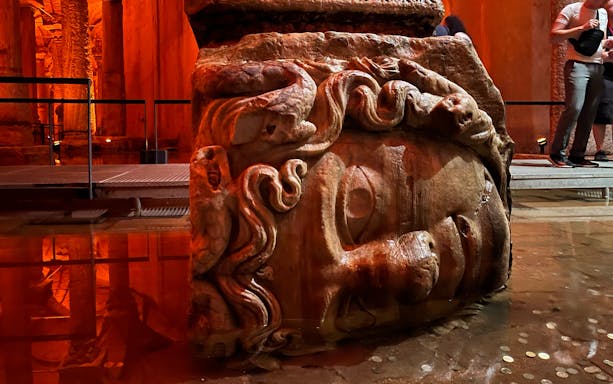 Medusa head column base in Basilica Cistern, Istanbul, with visitors nearby.