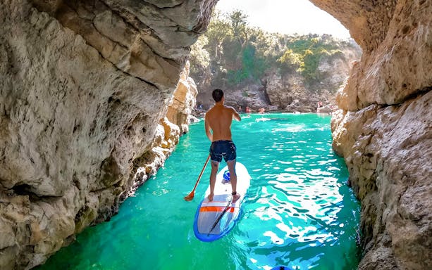 Paddle boarding through a rocky cave in Sorrento with turquoise water.