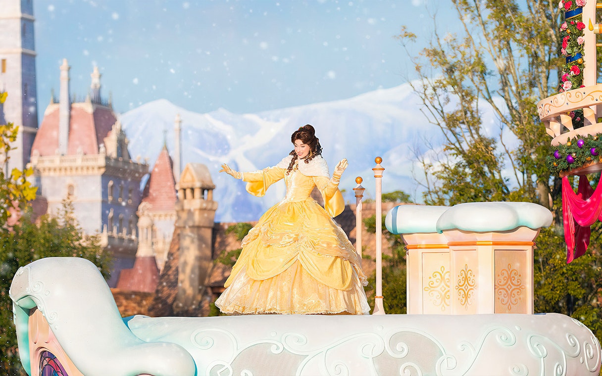 Character in yellow dress on float at Tokyo Disneyland with castle in background