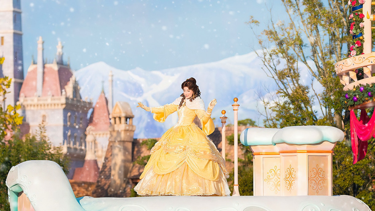 Character in yellow dress on float at Tokyo Disneyland with castle in background