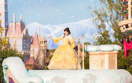 Character in yellow dress on float at Tokyo Disneyland with castle in background