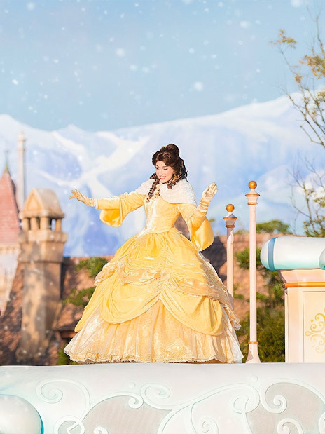 Character in yellow dress on float at Tokyo Disneyland with castle in background