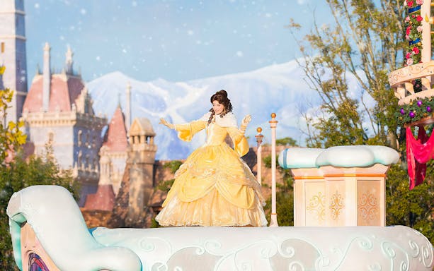 Character in yellow dress on float at Tokyo Disneyland with castle in background