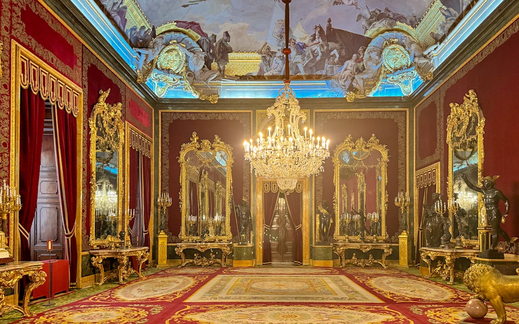 Royal Palace of Madrid room with ornate chandeliers, gilded mirrors, and red velvet decor.