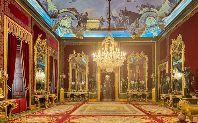 Royal Palace of Madrid room with ornate chandeliers, gilded mirrors, and red velvet decor.