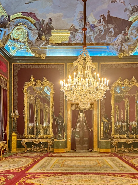 Royal Palace of Madrid room with ornate chandeliers, gilded mirrors, and red velvet decor.