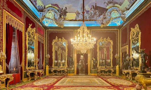 Royal Palace of Madrid room with ornate chandeliers, gilded mirrors, and red velvet decor.