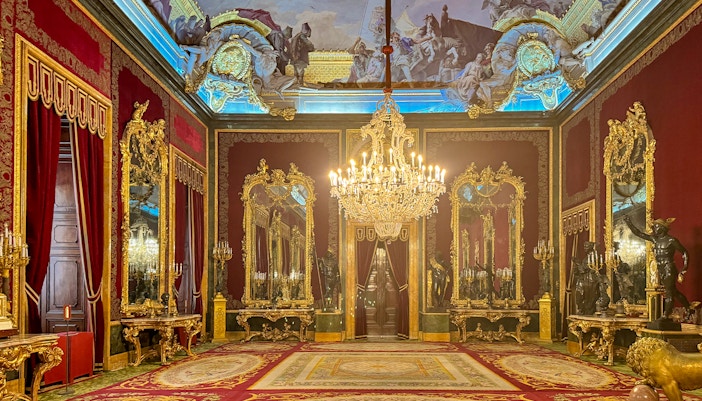 Royal Palace of Madrid room with ornate chandeliers, gilded mirrors, and red velvet decor.