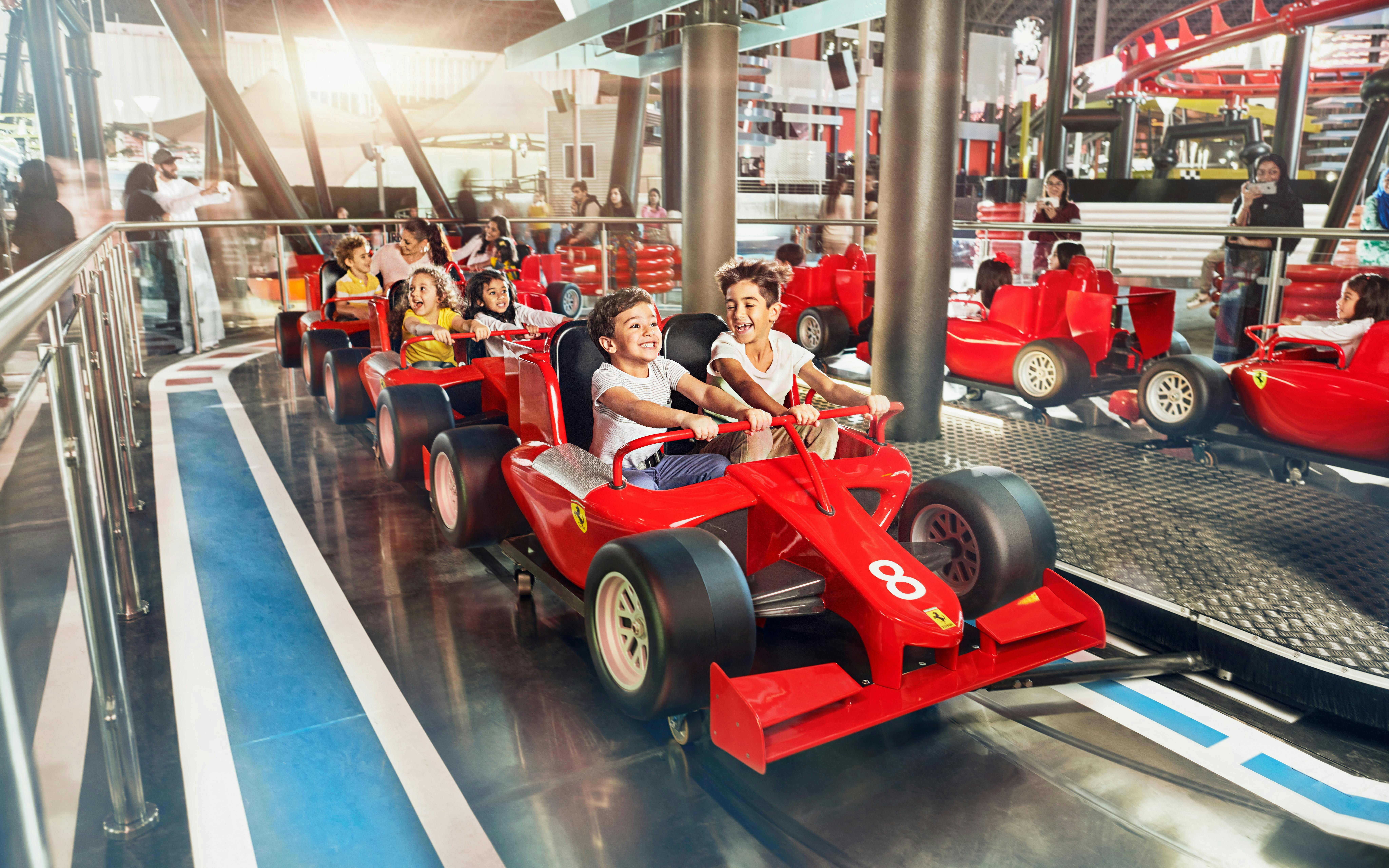 Children enjoying a ride in red race cars at Ferrari World Abu Dhabi.