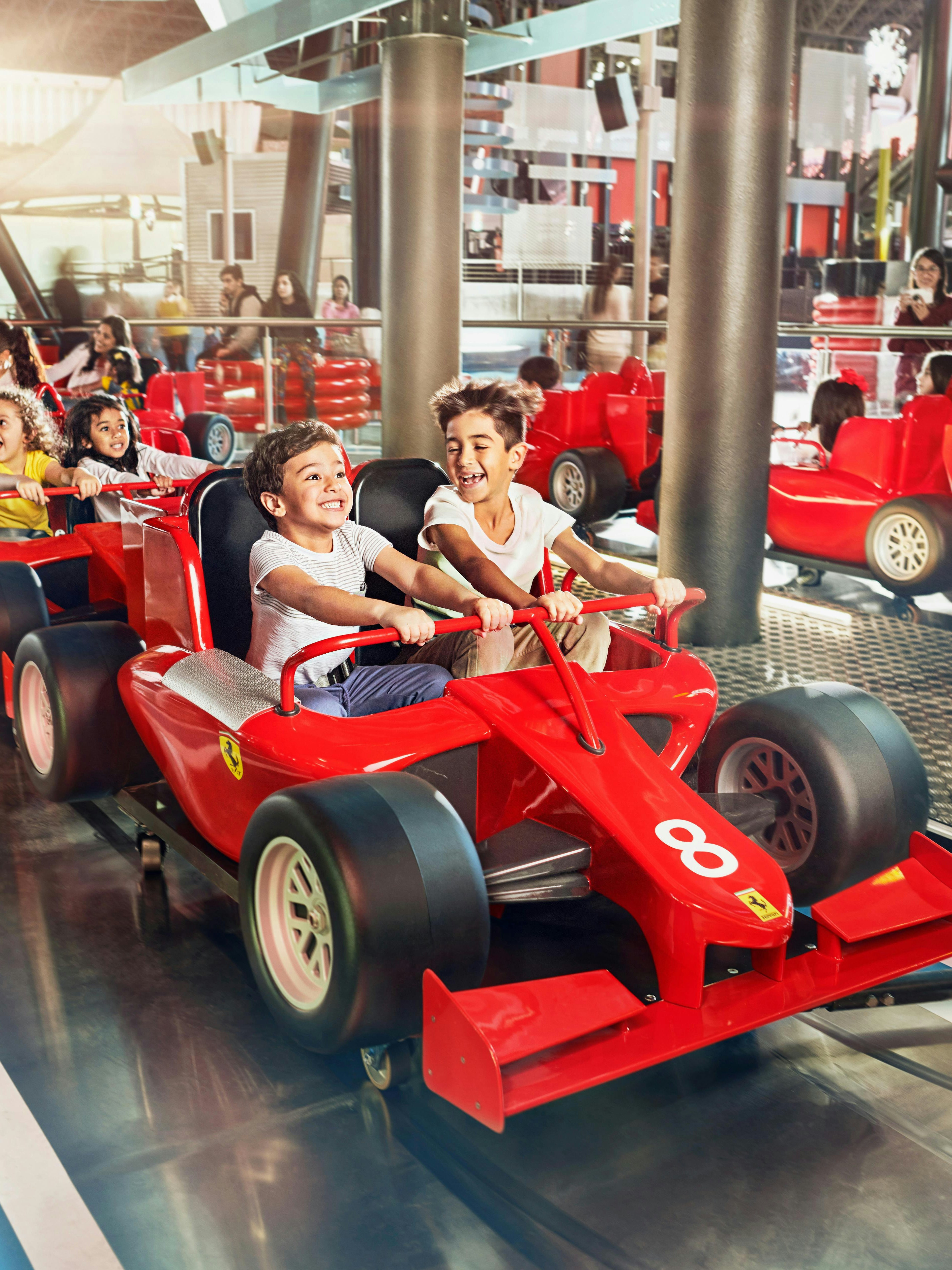 Children enjoying a ride in red race cars at Ferrari World Abu Dhabi.