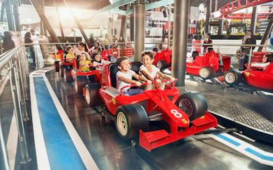 Children enjoying a ride in red race cars at Ferrari World Abu Dhabi.