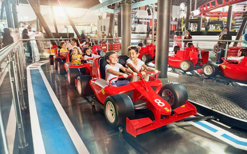 Children enjoying a ride in red race cars at Ferrari World Abu Dhabi.