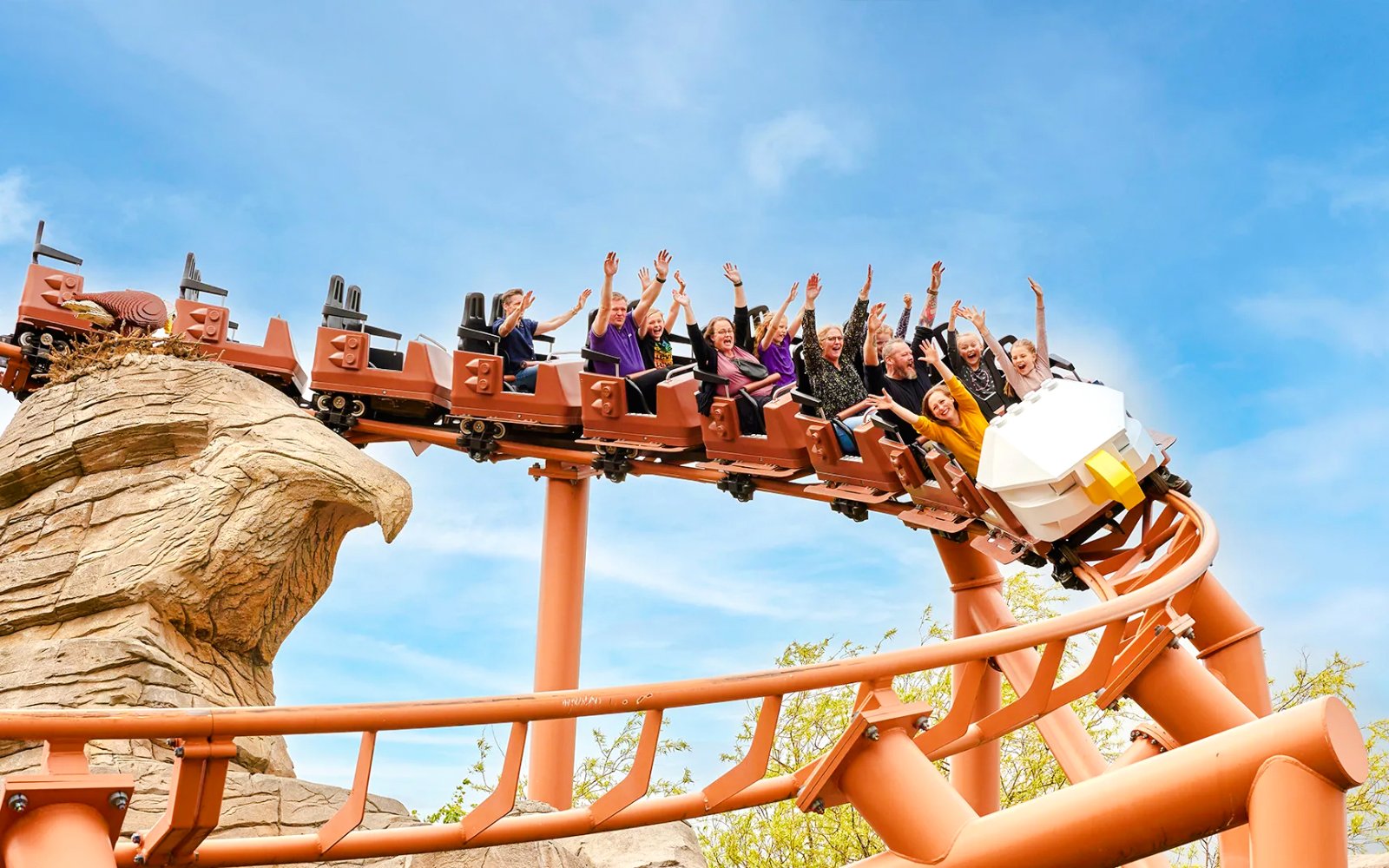 Visitors on a roller coaster at LEGOLAND Billund with hands raised in excitement.