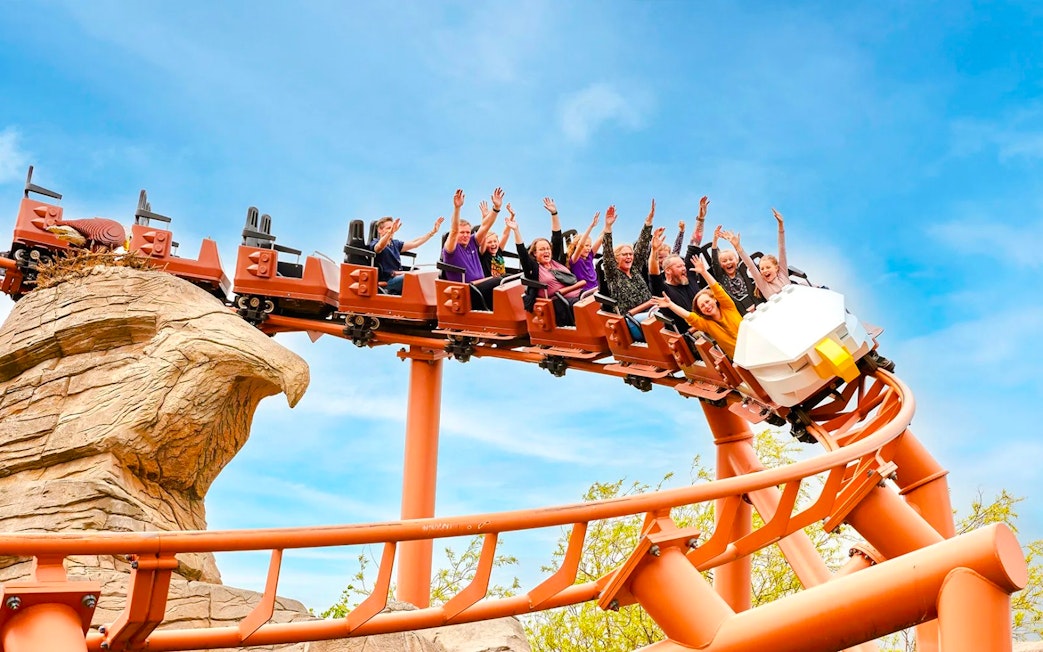 Visitors on a roller coaster at LEGOLAND Billund with hands raised in excitement.