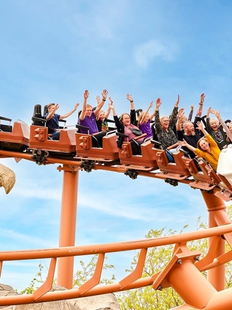 Visitors on a roller coaster at LEGOLAND Billund with hands raised in excitement.