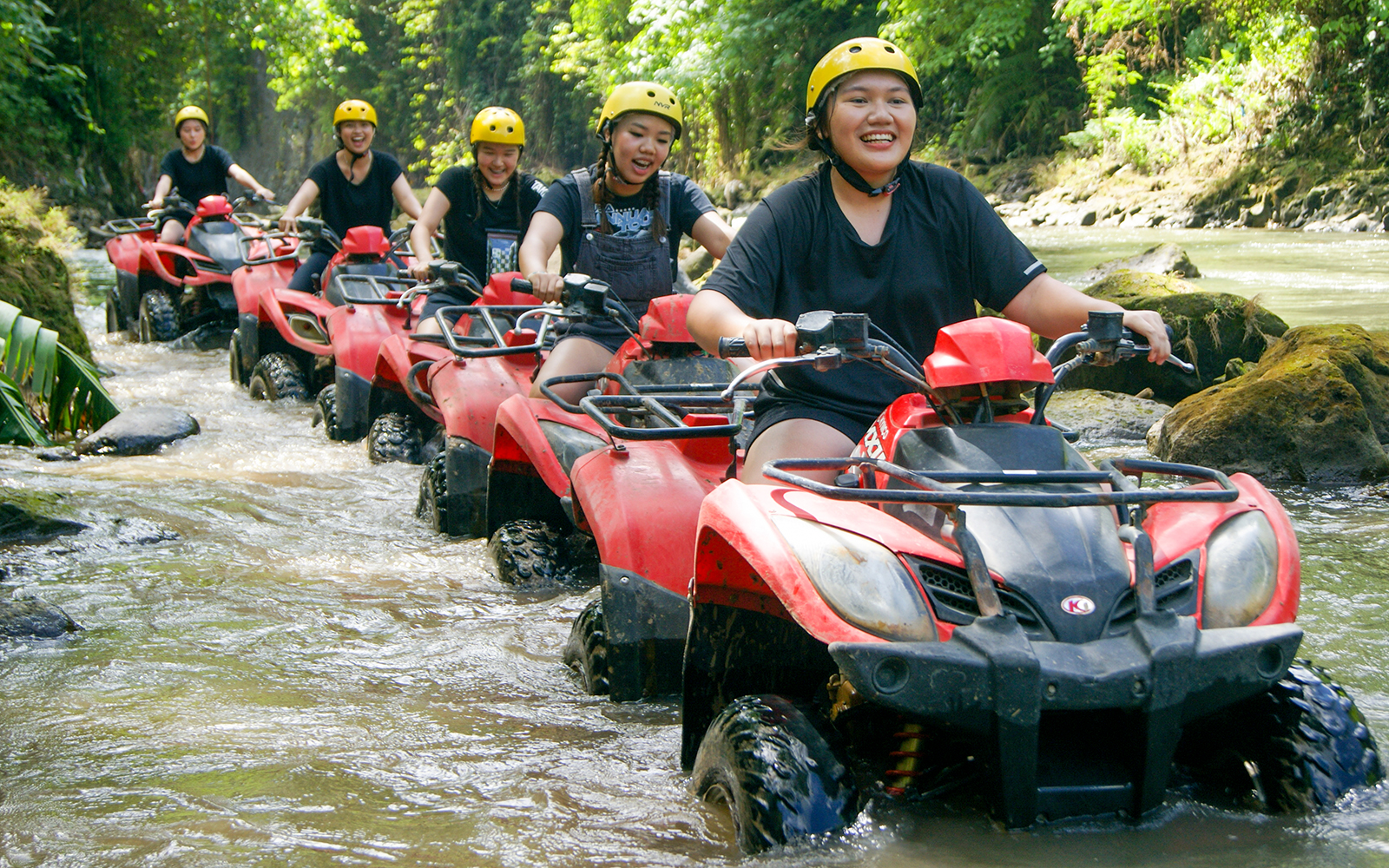 Group riding red ATVs through a forest stream on a Bali quad bike tour.