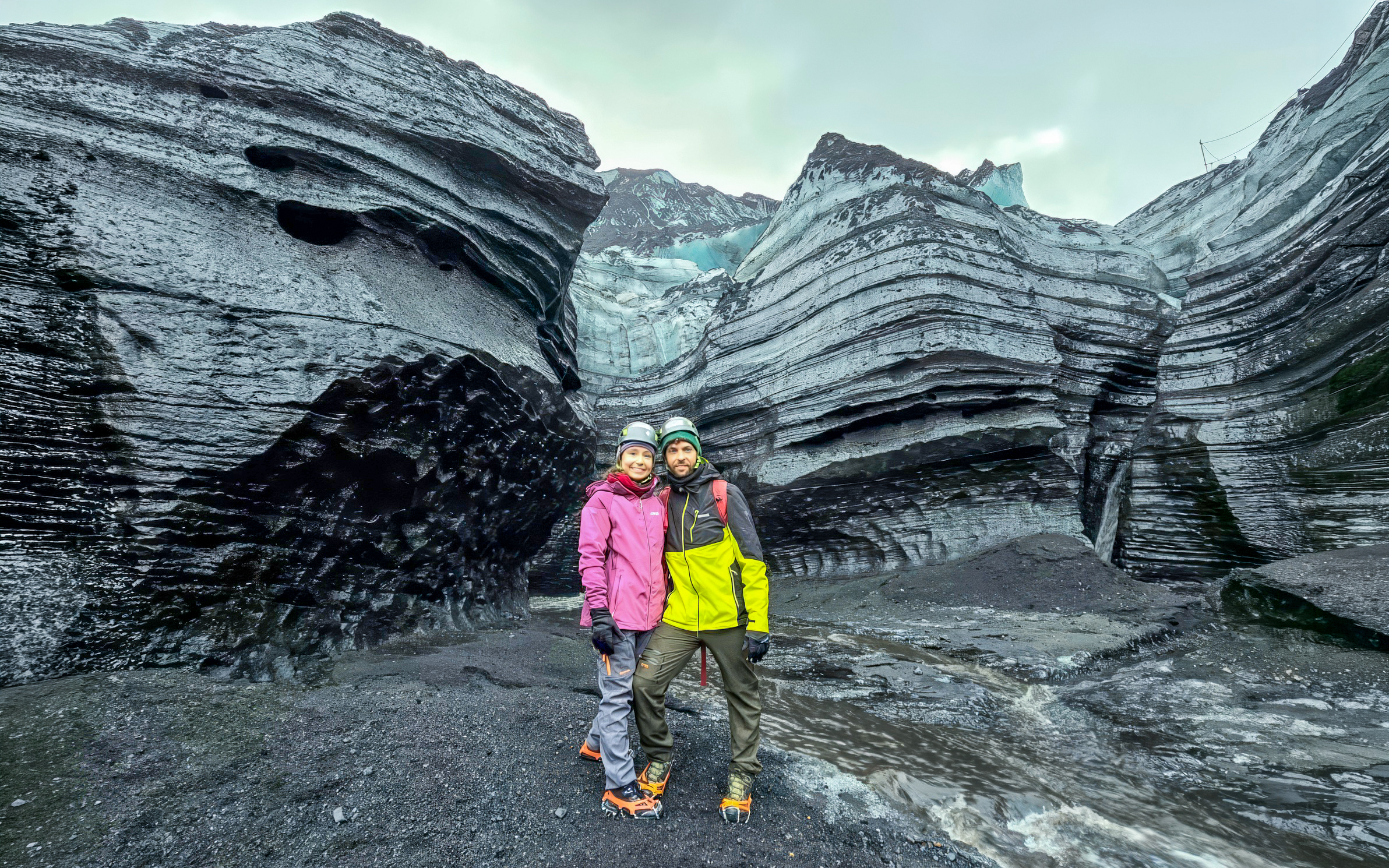 Visitors stand at the entrance of Katla Ice Cave, Iceland, surrounded by layered ice formations.