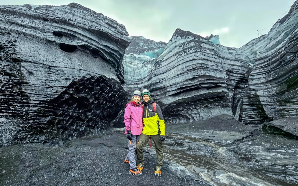 Visitors stand at the entrance of Katla Ice Cave, Iceland, surrounded by layered ice formations.