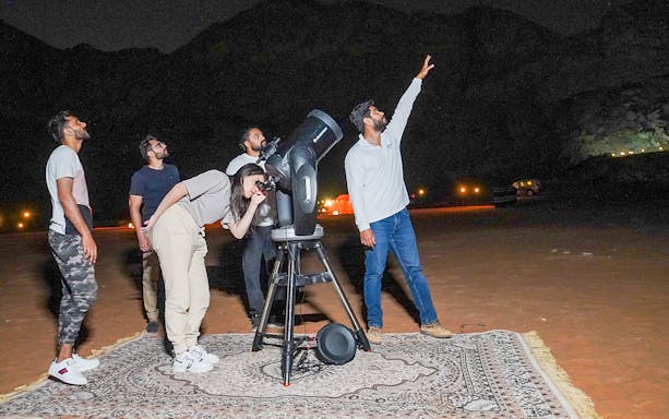 Group stargazing with telescope in Mleiha desert at night.